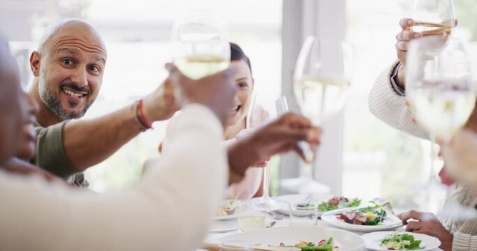 Group of friends saying cheers while lifting their wine glasses to share a toast during lunch around a table at home or a luxury hotel. Happy and diverse people eating food and celebrating friendship