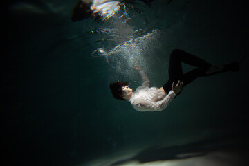 Sink. A young man is going to the bottom. A guy in a white shirt and trousers falls under the water, calmness and acceptance of fate - 513064936