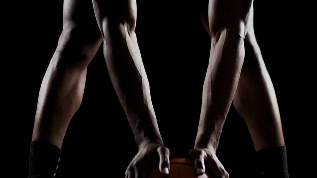 Basketball player resting on a ball. African american sports man practicing against black background. Abstract body shot front view..