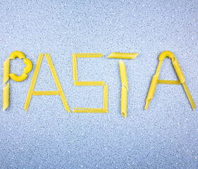 Pasta word. The word pasta laid out on a blue background with pasta. Penne and spaghetti. A variety of pasta assortment.