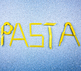 Pasta word. The word pasta laid out on a blue background with pasta. Penne and spaghetti. A variety of pasta assortment.