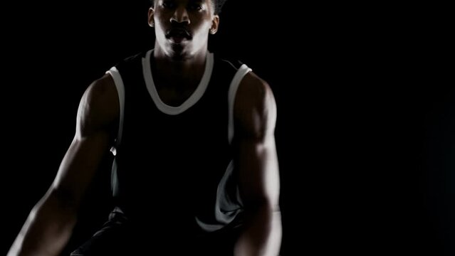 Basketball player bouncing a ball. African american sports man practicing against black background. Abstract upper body view.