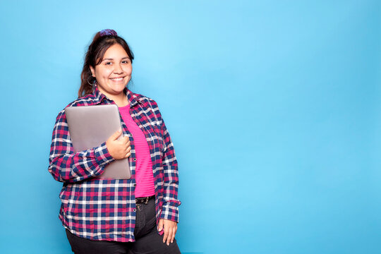 Young Curvy Latina Woman Smiling Holding Laptop Looking At Camera. Indoor Studio Shot Isolated On Blue Background.