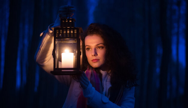 Young woman in the woods walking with lantern at night 