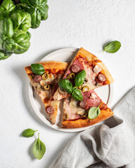 Three pieces of pizza in white plate, linen napkin and basil leaves on white table. Top view