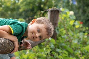 portrait of a little smiling boy in a green T-shirt stands near a wooden fence in nature