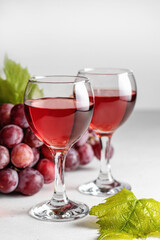 Two glasses of red wine and grapes on a light background