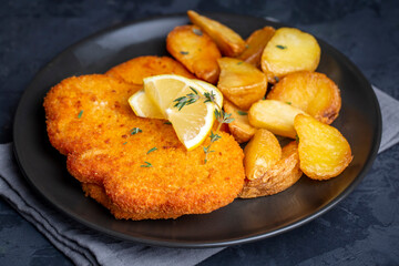 Chicken schnitzel with sauce, fried potatoes and lemon in a plate