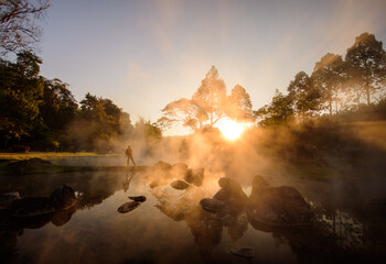 Chae Son National Park hot springs over rocky terrain Mist and morning sunlight shining through the branches of trees in the middle of nature, Lampang Province, Thailand.