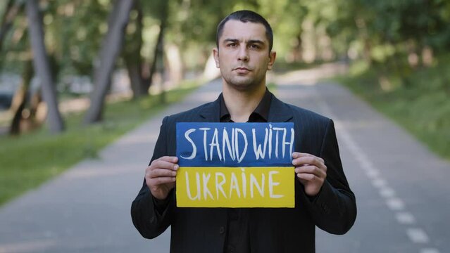 Portrait sad serious man activist patriot guy stand outdoors hold cardboard with written inscription stand with Ukraine protests against military conflict demonstrate opposition anti violence banner