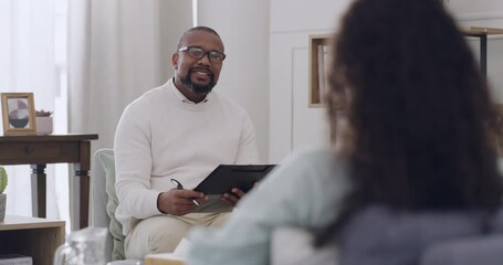 African male psychologist writing notes while listening to a female patient talk about issues and emotions during a therapy session. Young patient talking to her therapist about her problems.