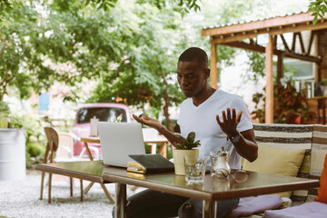 Surprised and confused african afro american man with laptop in cafe dont know what to do, throwing hands in outdoor cafe. Business and freelancing problems. Waiting results of online web meeting