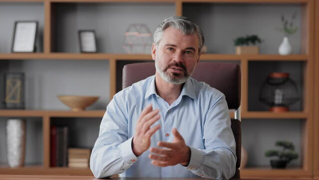Smiling businessman talking to web camera sitting in office. Recording vlog, online video conference, video call, online education. Job interview, online training. Webcam view.