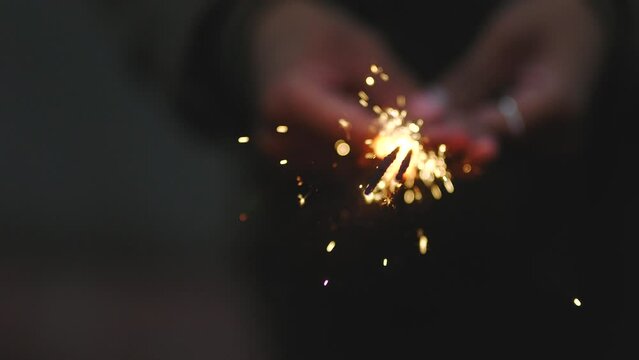 Closeup of a person holding and firing a sparkler in night celebration. Unrecognizable woman enjoying nightlife with a firecracker in evening. Festive person celebrating the holidays with fireworks