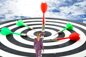 Businesswoman on board with color darts hitting target against cloudy sky