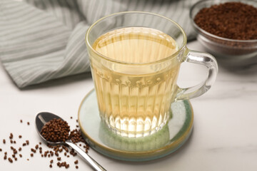 Glass cup of buckwheat tea and granules on white marble table