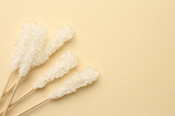Wooden sticks with sugar crystals and space for text on beige background, flat lay. Tasty rock candies