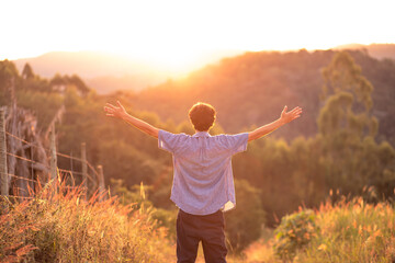 Young man with arms raised thanking God, with the sunset in the background. Concept of happiness and success.