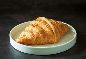 Closeup fresh croissant sprinkled with powdered sugar in a white plate on dark  background.