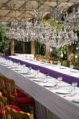 Glass goblets and glasses, white plates, cutlery for festive table setting for luxurious wedding or birthday party outdoors. Sun light. Soft focus.