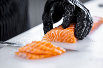 The salmon is in the hands of the experienced chef. He is using a knife to slice salmon fillet for...