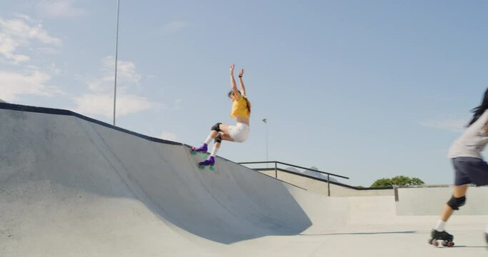 Full length of two friends rollerskating in skate park and rink. Cool young fun people performing skating tricks outside. Happy mixed race man and woman bonding enjoying free time on weekend and hobby