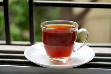FULL CUP RED LIQUOR TEA IN TRANSPARENT IN WINDOW AS MORNING TEA