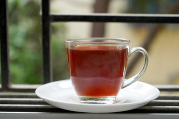 Fototapeta premium TRANSPARENT CUP WITH RED LIQUOR TEA BESIDE THE WINDOW