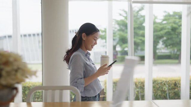 Asia people digital nomad adult female relax smile read social media app online chat text message look at mobile phone hold takeaway hot drink to-go zero waste cup enjoy coffee break at office outside