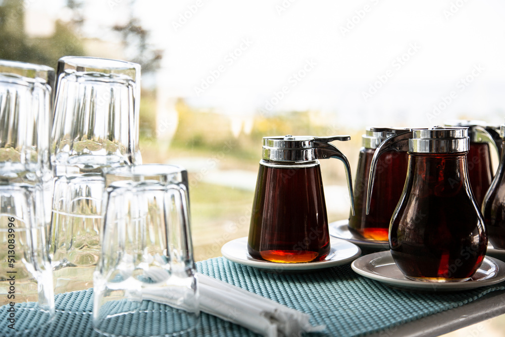 Wall mural amber maple syrup in glass serving dispensers on saucers next to glassware by a window.