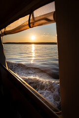 Sunset over the sea from the window of a boat moving through the water.