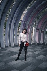 futuristic portrait of a generation z girl with black hair, sunglasses, red bag, white t-shirt and black pants gesturing on a metallic and modernist background