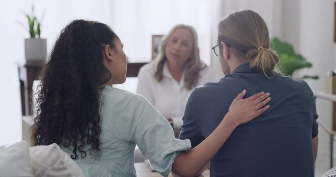 A young interracial couple comforting each other during a therapy session with their mature female therapist in an office. Unhappy couple trying to resolve issues in their relationship, before divorce