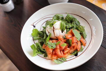 Caprese salad in a round white plate. on a modern wooden table. Selective focus.