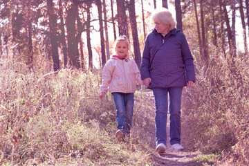 Happy grandmother with granddaughter together. Walking along autumn or winter path