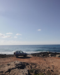 Car is parked at the edge near the sea in sunny day.