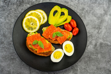 Toast with salmon and avocado on a black plate.