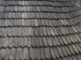 Old wood shingle roof with rough surface, background. Wooden planks on the top of a building. Weathered tiles on the roof. The texture of dark wood in the form of wooden tiles.