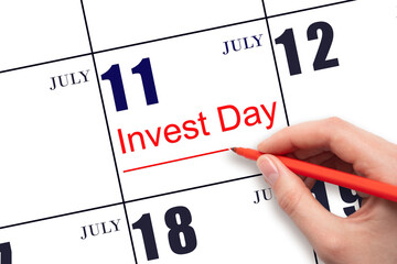 Hand drawing red line and writing the text Invest Day on calendar date July 11. Business and financial concept.