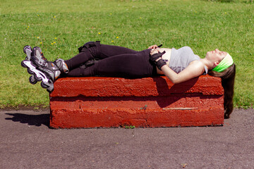 Sporty young woman stretching and resting after skating in a park on a sunny day