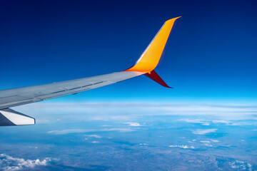 Airplane wing flying high in the atmosphere against the background of blue air. White-orange plane...