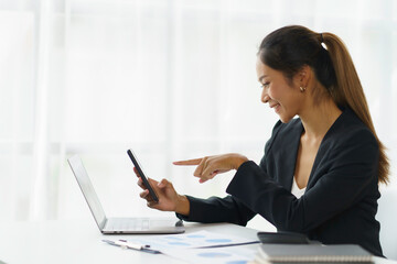Beautiful young Asian businesswoman with a smile sitting using smartphone at the office.