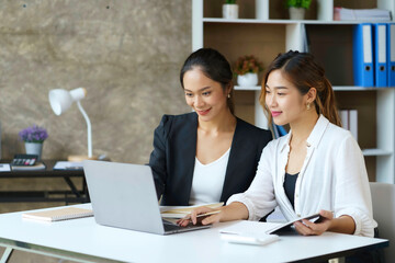 Two young Asian professional businesswomen working talking in a modern startup with laptop computer at the office..