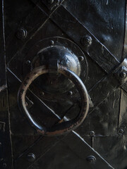 The ring of an old medieval door. Heavy metal door. Art wall decor iron pattern for background. The black door is decorated with geometric patterns with steel stripes.