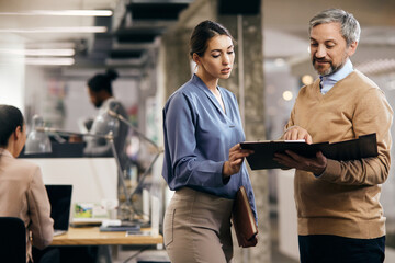 Mature businessman and his female colleague analyzing paperwork while working at corporate office.