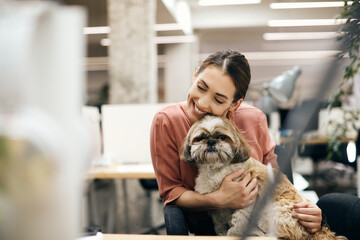 Happy businesswoman cuddling her dog while working in pet friendly office.