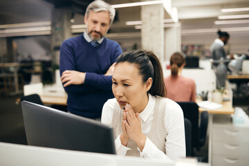 Pensive Asian businessman reading e-mail on computer in office.