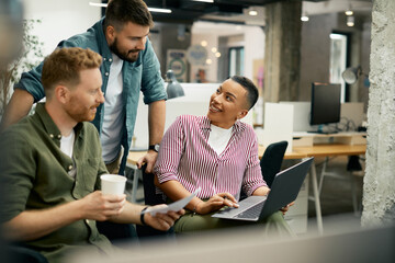 Young happy entrepreneurs cooperating while working on laptop in office.