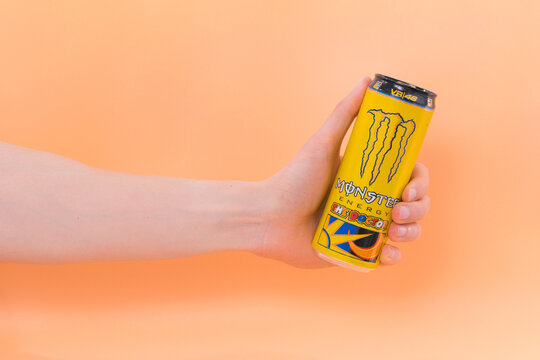 Corona, USA - Feb 5 2022: Male hand holds a yellow can of Monster Energy Drink the doctor on orange background. Caffeine drinks. Favor. Health. Blend. Soda