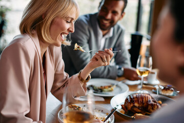 Happy businesswoman laughs while eating lunch with her colleagues in restaurant.